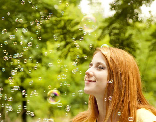 Rusovláska dívka v parku pod mýdlová bublina déšť. — Stock fotografie