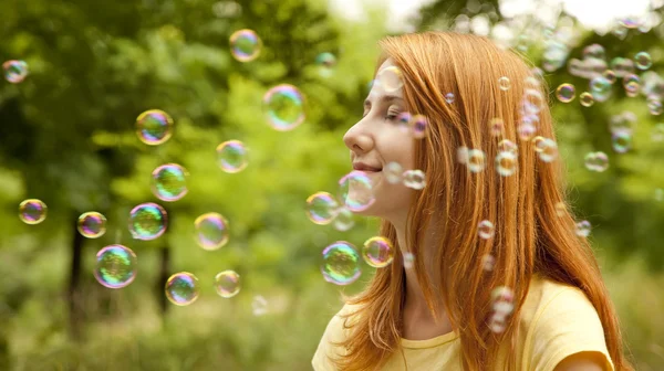 Pelirroja en el parque bajo la lluvia de jabón burbuja . —  Fotos de Stock