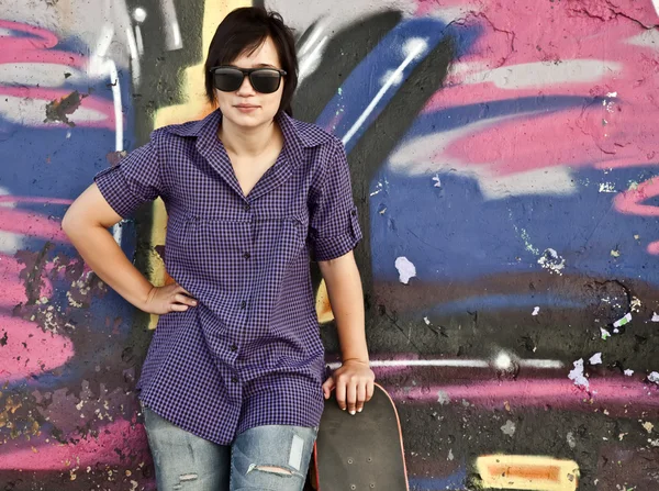 Chica de estilo con monopatín cerca de la pared de graffiti . —  Fotos de Stock