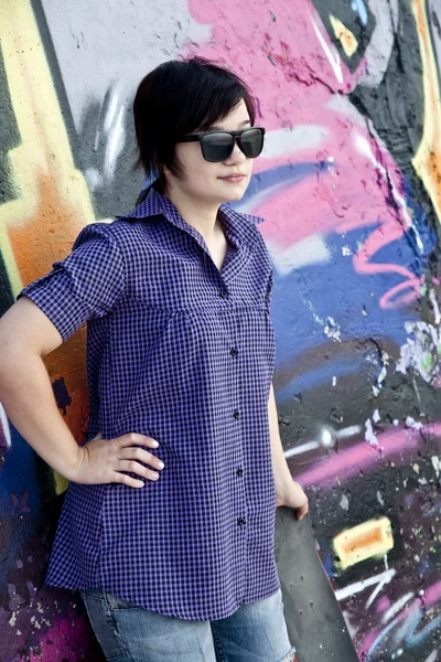 Style fille avec planche à roulettes près du mur de graffiti . — Photo