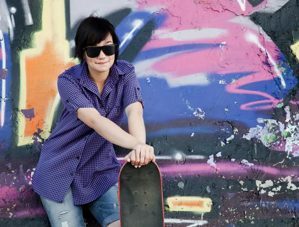 Styl dívka s skateboard poblíž graffiti zeď. — Stock fotografie