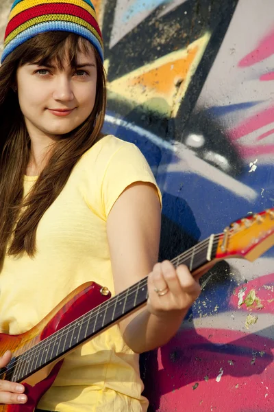Девушка-брюнетка с гитарой и стеной на заднем плане — стоковое фото