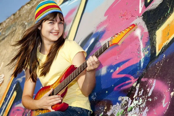 Девушка-брюнетка с гитарой и стеной на заднем плане — стоковое фото