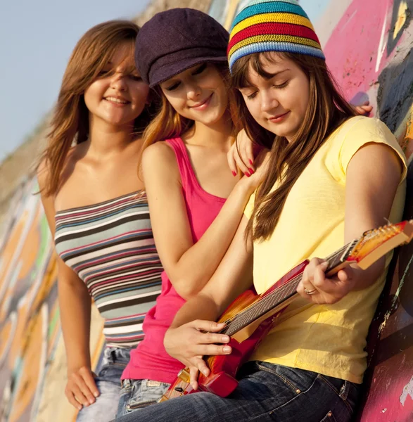Three beautiful girls with guitar and graffiti wall at backgroun — Stock Photo, Image
