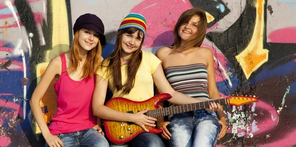 Three beautiful girls with guitar and graffiti wall at backgroun — Stock Photo, Image
