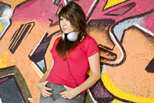 Beautiful brunette girl with headphones and graffiti wall at bac — Stock Photo, Image