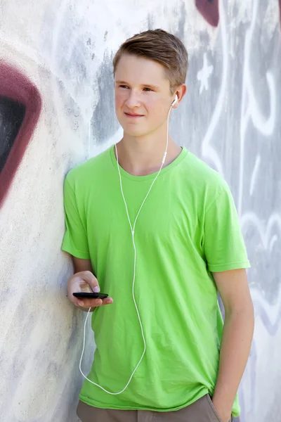 Tiener jongen met koptelefoon in de buurt van graffiti muur. — Stockfoto
