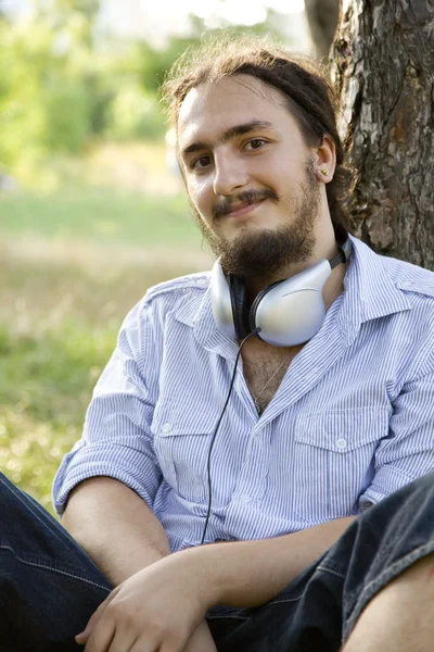 Mann sitzt mit Kopfhörern auf grünem Gras. — Stockfoto