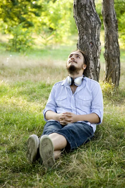 Homem sentado na grama verde com fones de ouvido . — Fotografia de Stock