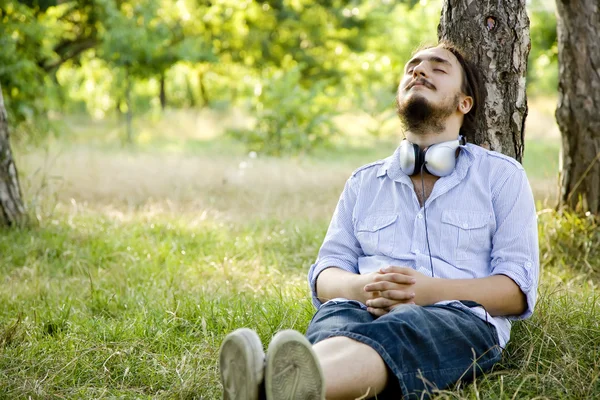 ヘッドフォンで緑の草に坐っている人. — ストック写真