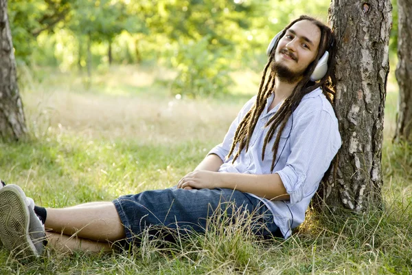 stock image Man sitting on green grass with headphones.