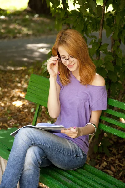 Redhead girl in glasses doing homework at the park. — Stock Photo, Image