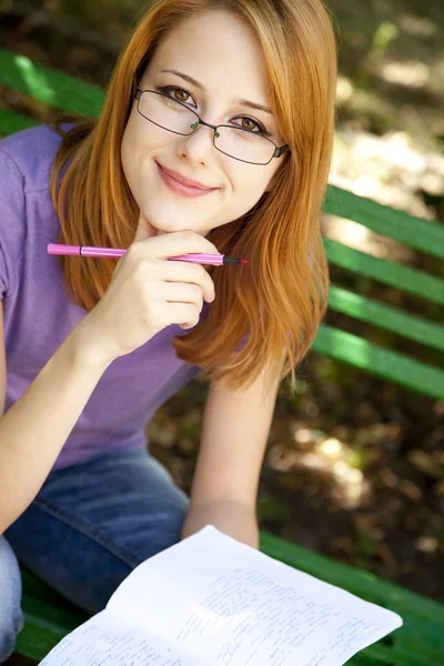 Pelirroja con gafas haciendo deberes en el parque . — Foto de Stock