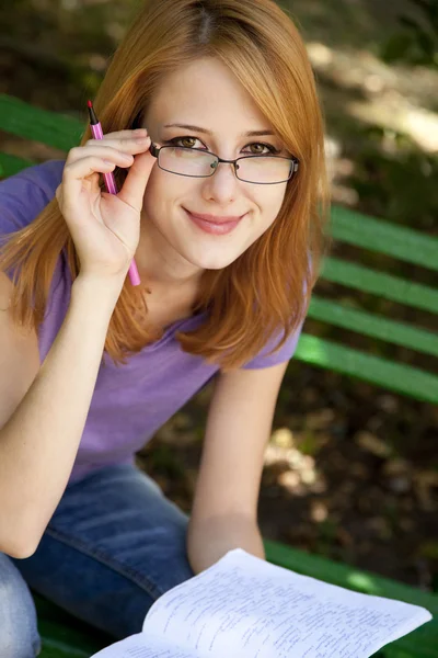 Redhead girl in glasses doing homework at the park. — Stock Photo, Image