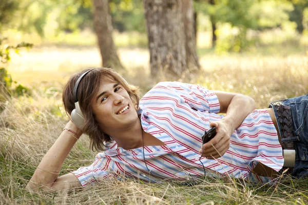 Usměvavý pohledný muž se sluchátky v přírodě — Stock fotografie