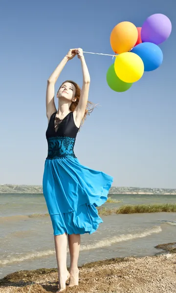 Rusovláska dívka s barevné balónky na pobřeží. — Stock fotografie