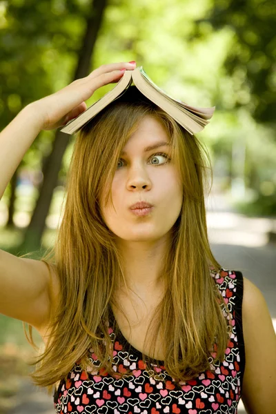Ξανθό κορίτσι με βιβλίο πάνω από το κεφάλι στο πάρκο. — Φωτογραφία Αρχείου
