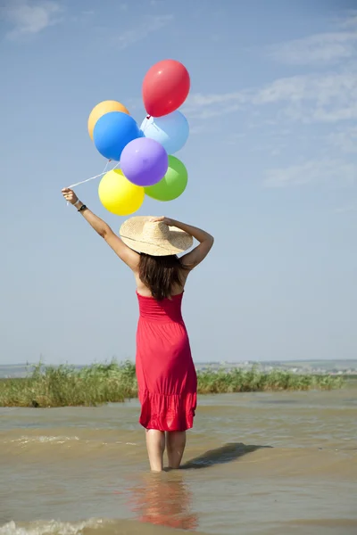 Brünettes Mädchen mit bunten Luftballons an der Küste. — Stockfoto