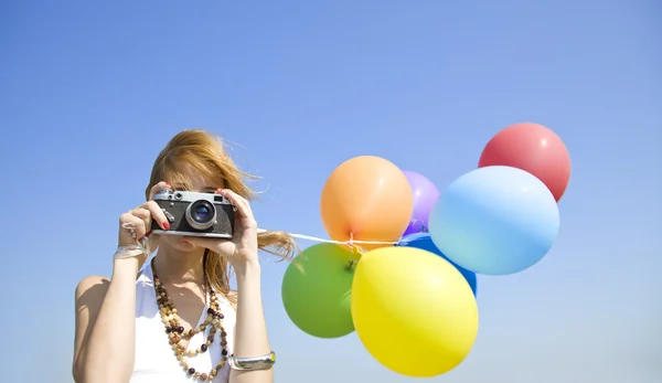 Ragazza rossa con palloncini a colori e fotocamera a cielo blu backgro — Foto Stock
