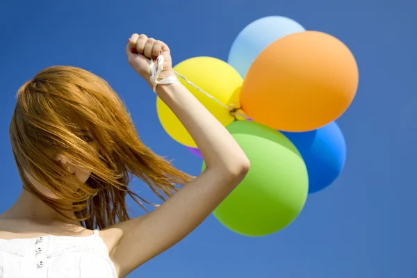 Rödhårig tjej med färg ballonger på blå himmel bakgrund. — Stockfoto