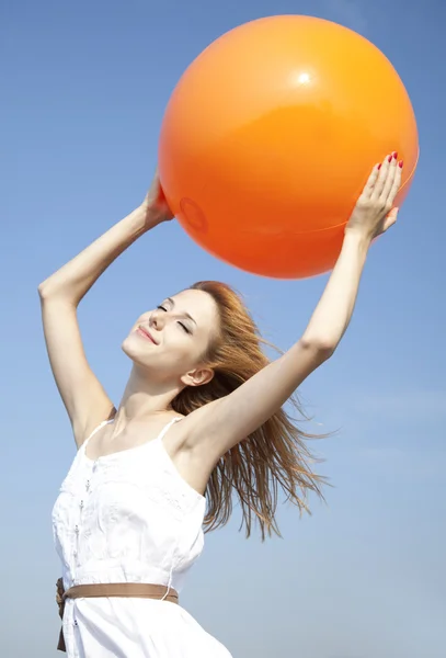 Рыжая девушка держит мяч на голубом фоне неба . — стоковое фото