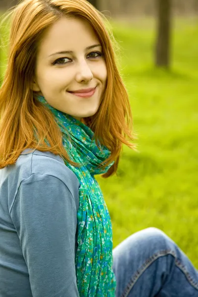 Hermosa chica pelirroja sentada en la hierba verde en el parque . —  Fotos de Stock
