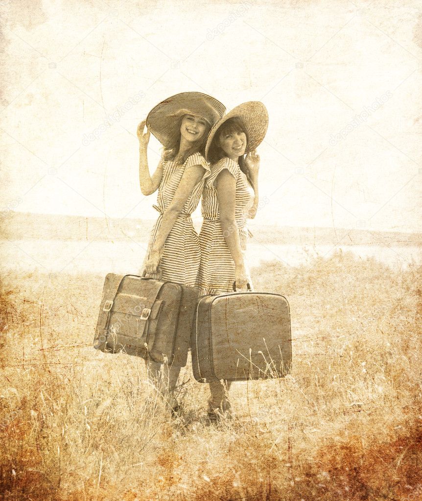 Two retro style girls with suitcases at countryside.