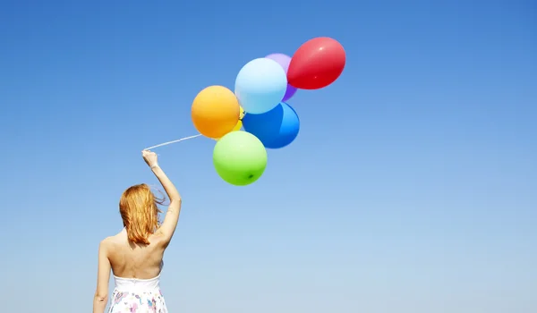 Rödhårig tjej med färg ballonger på blå himmel bakgrund. — Stockfoto