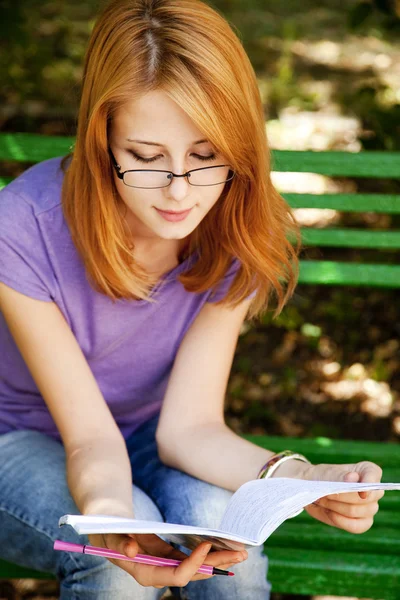 Rothaarige Mädchen mit Brille machen Hausaufgaben im Park. — Stockfoto
