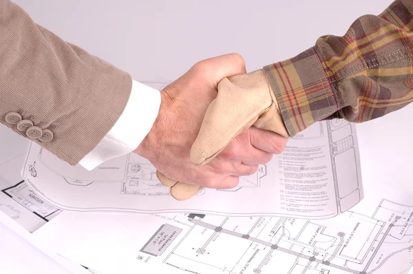 Рабочий и бизнесмен пожимает руку над планами ремонта дома — стоковое фото