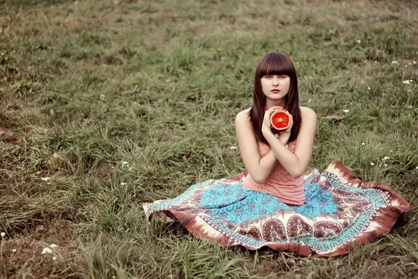 Vacker flicka i en lång kjol med grapefrukt i parken — Stockfoto