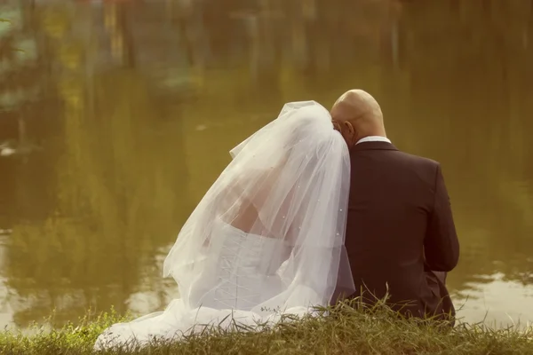 La novia y el novio se sientan en la orilla del lago —  Fotos de Stock