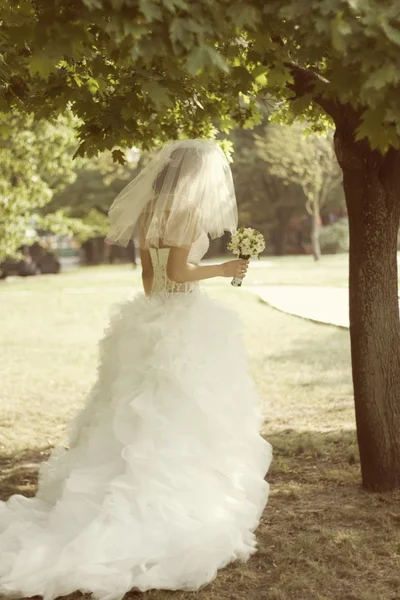 La novia con un ramo en un parque cerca de un árbol — Foto de Stock