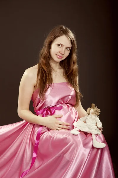 Hermosa chica embarazada en un vestido rosa con el juguete de un niño — Foto de Stock