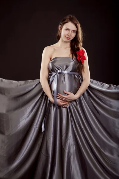 Mujer embarazada en un vestido gris con una flor roja en el pelo — Foto de Stock