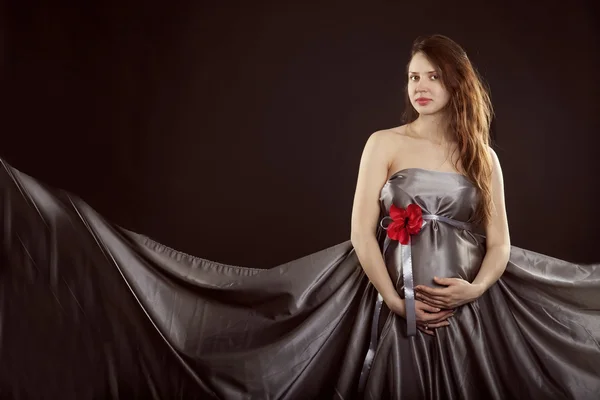 Gravid kvinna i en grå klänning med en röd blomma — Stockfoto