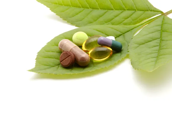 Vitaminas, tabletas y pastillas en hoja verde — Foto de Stock