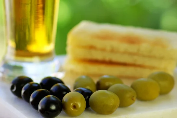 Glass of cold beer with olives on green background — Stock Photo, Image