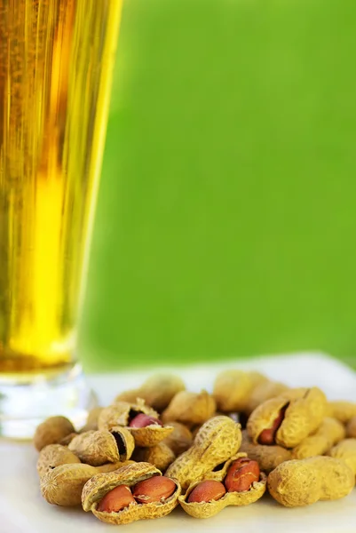 Стакан холодного пива с арахисом на зеленом фоне — стоковое фото