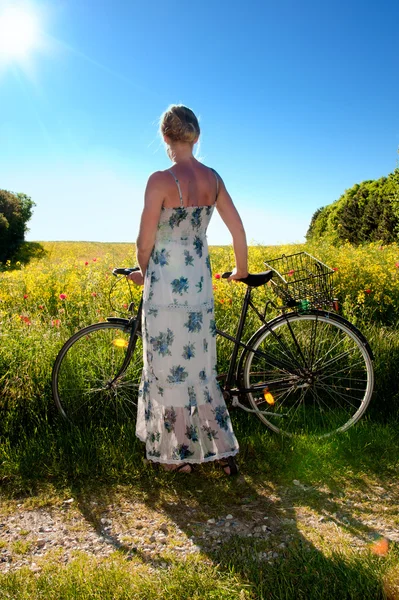 Atractiva joven con una bicicleta se detiene en el borde de un campo de colza — Foto de Stock