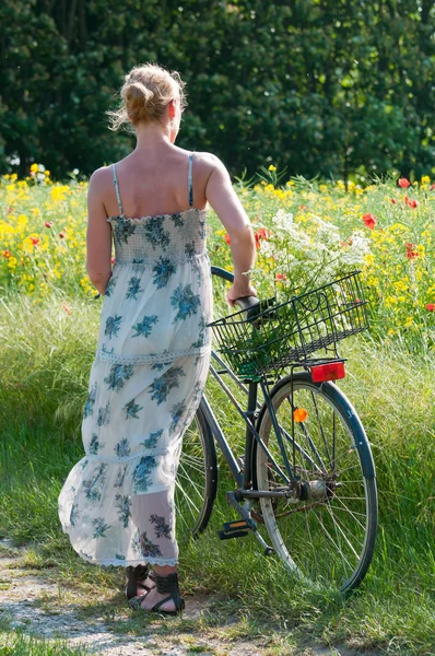 Ελκυστική νεαρή γυναίκα με ένα ποδήλατο παύσεις στην άκρη ενός πεδίου αγριογογγύλης ή/και Royalty Free Εικόνες Αρχείου