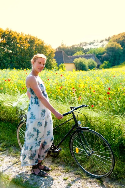 Ελκυστική νεαρή γυναίκα με ένα ποδήλατο παύσεις στην άκρη ενός πεδίου αγριογογγύλης ή/και Εικόνα Αρχείου
