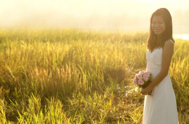 Asian bride at outdoor in a morning surrounding by golden sunlig clipart