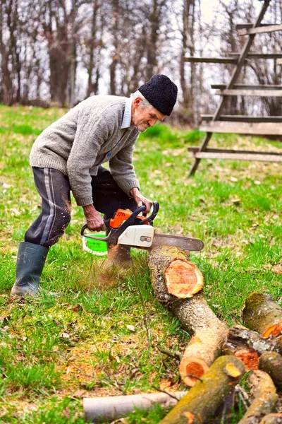 Old farmer with chainsaw cutting a tree — Zdjęcie stockowe