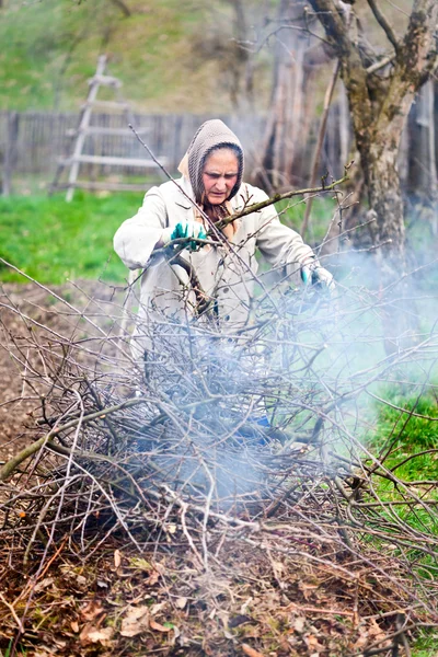 Senior landsbygdens kvinna bränna grenar och kvistar — Stockfoto