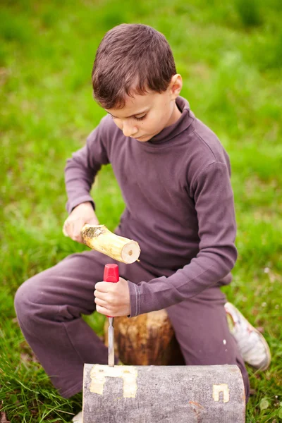 Мальчик лепит в бревне зубилом — стоковое фото