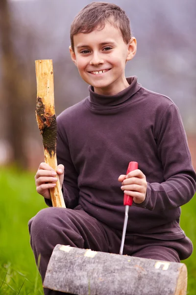 Ragazzo che scolpisce in un tronco con uno scalpello — Foto Stock