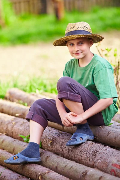 Счастливый мальчик на свежем воздухе, сидя на сосновых бревнах — стоковое фото