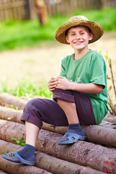Lycklig pojke utomhus sitter på tall stockar — Stockfoto