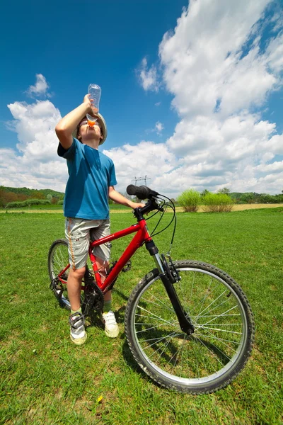 Boy on a bicycle drinking water — Stock Photo, Image